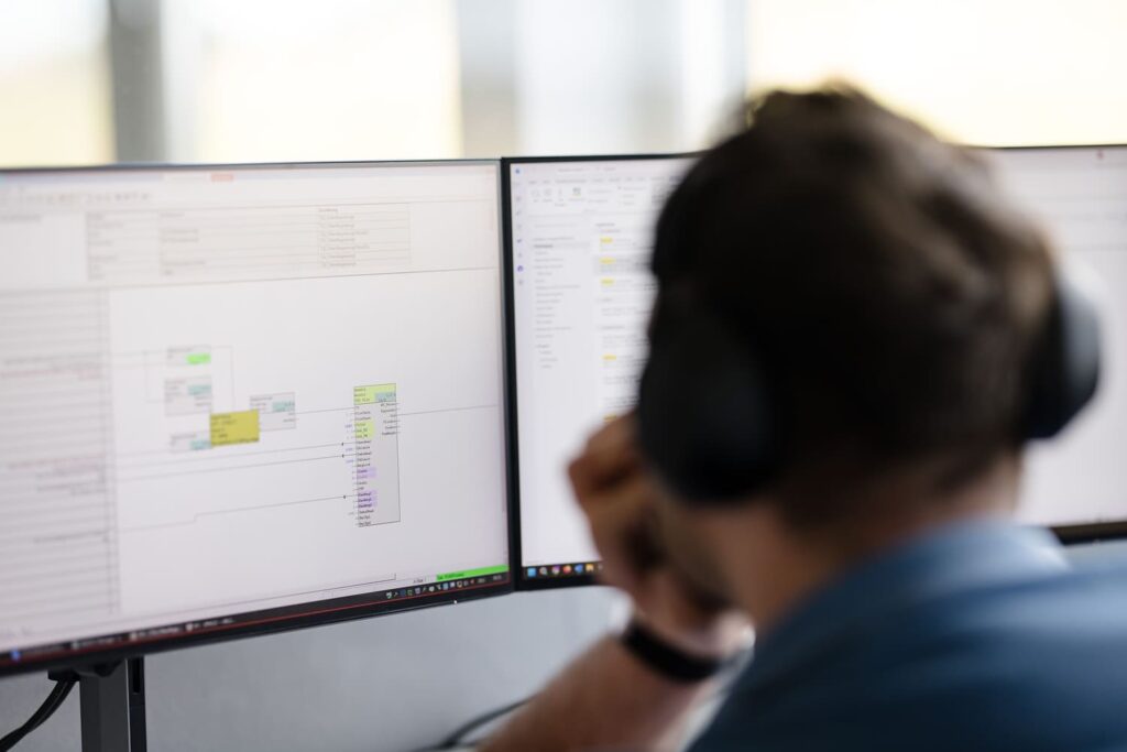Person mit Headset am Arbeitsplatz mit mehreren Bildschirmen